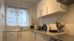 Et lille køkken med hvide skabe, en mikrobølgeovn, en kaffemaskine og en komfur.