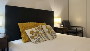 Et hotelværelse med en seng, et natbord, en lampe og en stol.