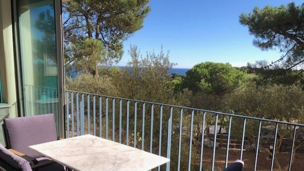 En balkon med et bord og stole, der udover et naturskønt udsyn til træer og havet.