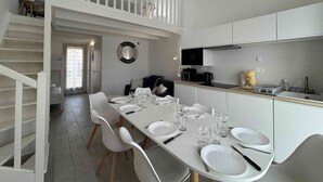 Een moderne keuken met witte kastjes, een eethoek met witte stoelen en een trap naar een hoger gelegen verdieping.