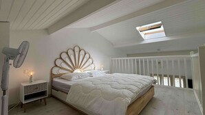 Een slaapkamer met een bed, nachtkastje, ventilator en dakraam.