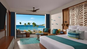 A hotel room with a large bed, a desk, a chair, a small table, and a view of the beach and ocean. - Dreams Macao Beach Punta Cana (Punta Cana)