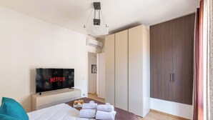 Un dormitorio con cama, un televisor que muestra 'NETFLIX', un armario y un baño al fondo.