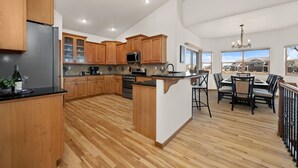A spacious kitchen with wooden cabinets, a central island, and a dining area with a view. - Cabin-style Group Retreat Near Rmnp, Lakes & Golf (Loveland)
