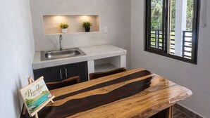 A compact kitchen with a wooden dining table, a small sink, and a window with a view of greenery.