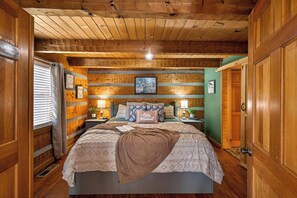 Un dormitorio acogedor con techo de madera, una cama con colcha, dos mesitas de noche con lámparas y un cuadro enmarcado en la pared.