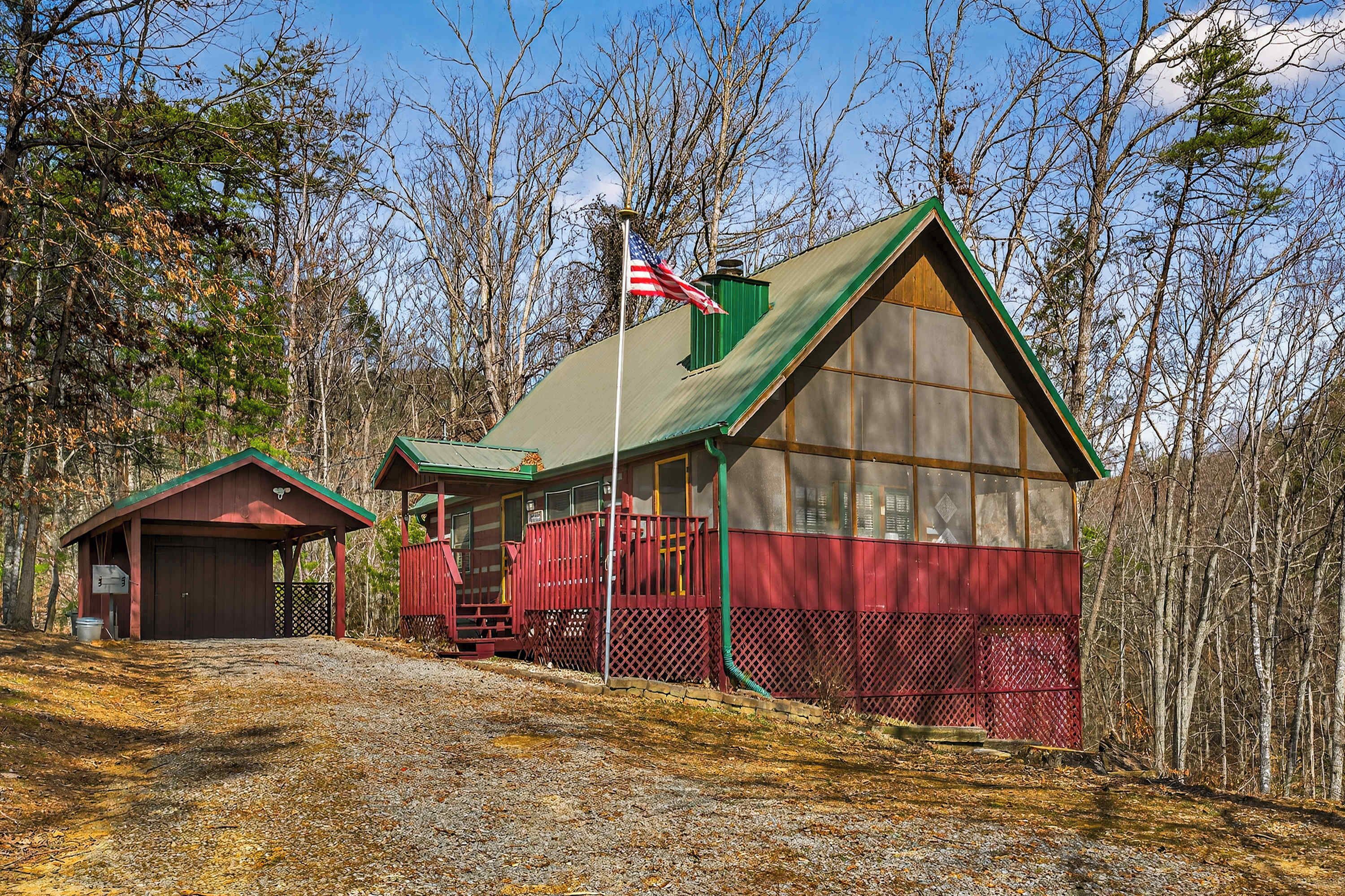 A cabin with a green roof, a red exterior, and a flagpole with an American flag.