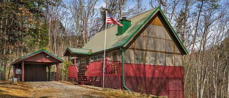A cabin with a green roof, a red exterior, and a flagpole with an American flag.
