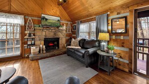 Un intérieur de chalet chaleureux avec une cheminée en pierre, un canapé en cuir et des murs en bois.