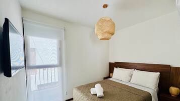 Ein Schlafzimmer mit einem Bett, einer Pendelleuchte, einem Fenster und einem an der Wand befestigten Fernseher.