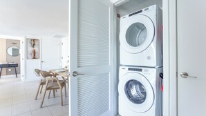 Un lavadero con lavadora y secadora apiladas, un comedor con sillas y una mesa, y una puerta que da a otra habitación.