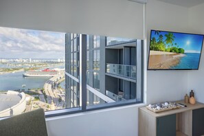 Une chambre moderne dotée d’une grande fenêtre donnant sur la ville, d’un téléviseur à écran plat fixé au mur et d’une table d’appoint en bois agrémentée d’objets décoratifs.