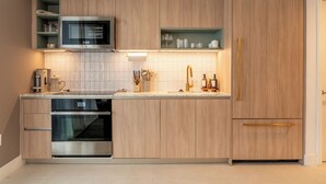 Una cocina moderna con armarios de madera, microondas integrado, horno de acero inoxidable y encimera con diversos utensilios de cocina.
