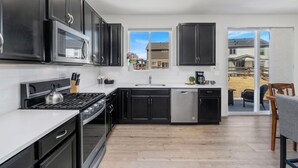 A modern kitchen with black cabinets, stainless steel appliances, and a large window offering a view of the backyard.