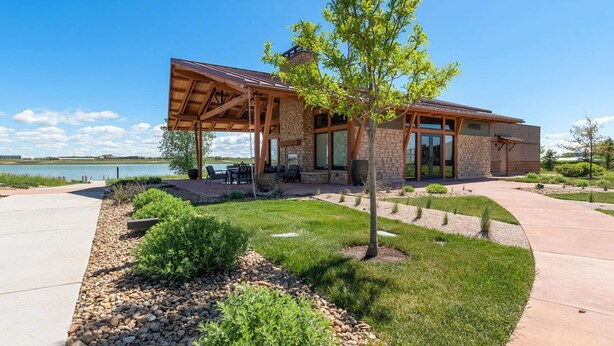 A modern building with a covered patio, stone walls, and a view of a lake.