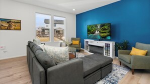 A modern living room with a grey sectional sofa, a green armchair, and a television mounted on a blue wall.