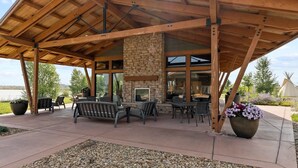 An outdoor patio with wooden beams, stone fireplace, and seating area.