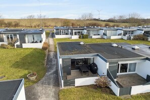 A row of modern mobile homes with flat roofs, a paved driveway, and a grassy area.
