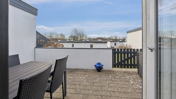 A patio with a table and chairs, a blue pot, and a gate. - Cosy small holiday apartment for 4 persons (Tranekær)