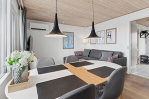 En moderne stue med spisebord, grå sofa og hængende lamper.