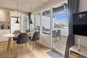 Une cuisine moderne avec un coin repas, de grandes portes-fenêtres coulissantes donnant sur un balcon et un téléviseur posé sur un meuble.