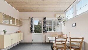 Een kamer met een eettafel, stoelen, een kast, een radiator en een raam met gordijnen.