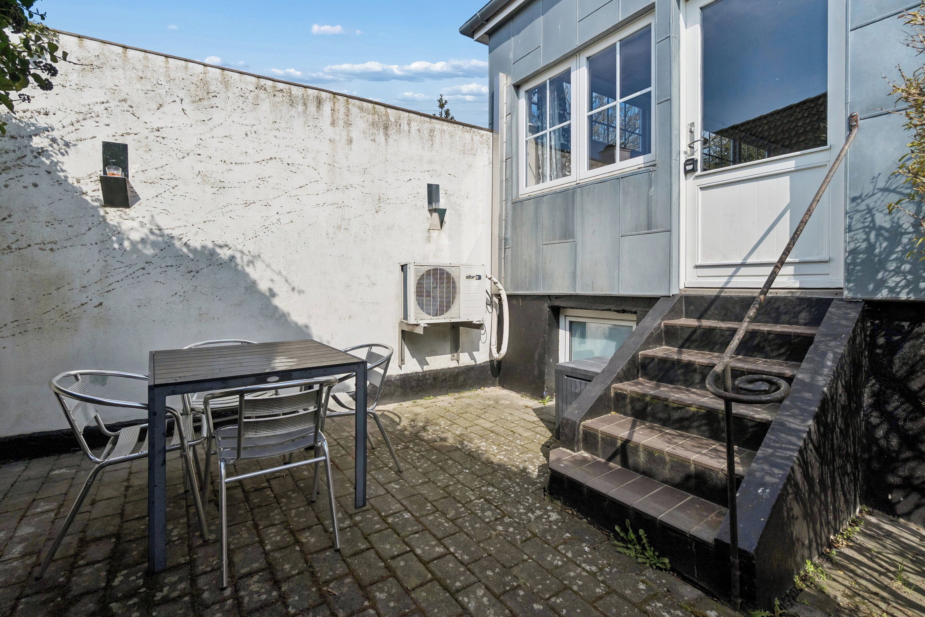 A patio with a table and chairs, a white wall, and a staircase leading to a door.
