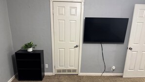 A room with a white door, a black entertainment unit, a plant, and a flat-screen TV mounted on the wall.
