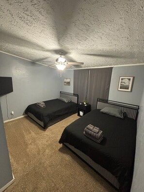 Une chambre avec deux lits, un ventilateur de plafond, une télévision et une petite table sur laquelle est posée une plante.
