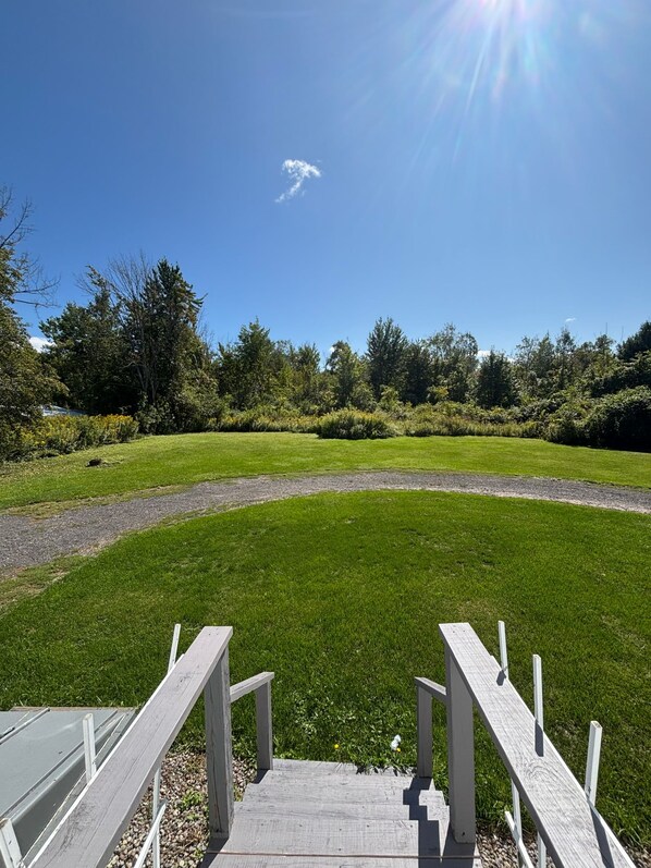 Une terrasse en bois qui mène à une zone herbeuse, avec un ciel dégagé.