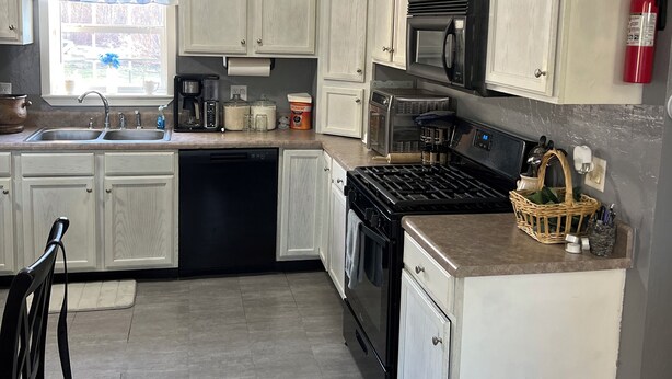 A kitchen with white cabinets, a stove, a microwave, and a sink.