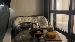 Un rincón acogedor con un banco acolchado, una mesa de cristal con copas de vino, un bol de aperitivos y una tabla de quesos.