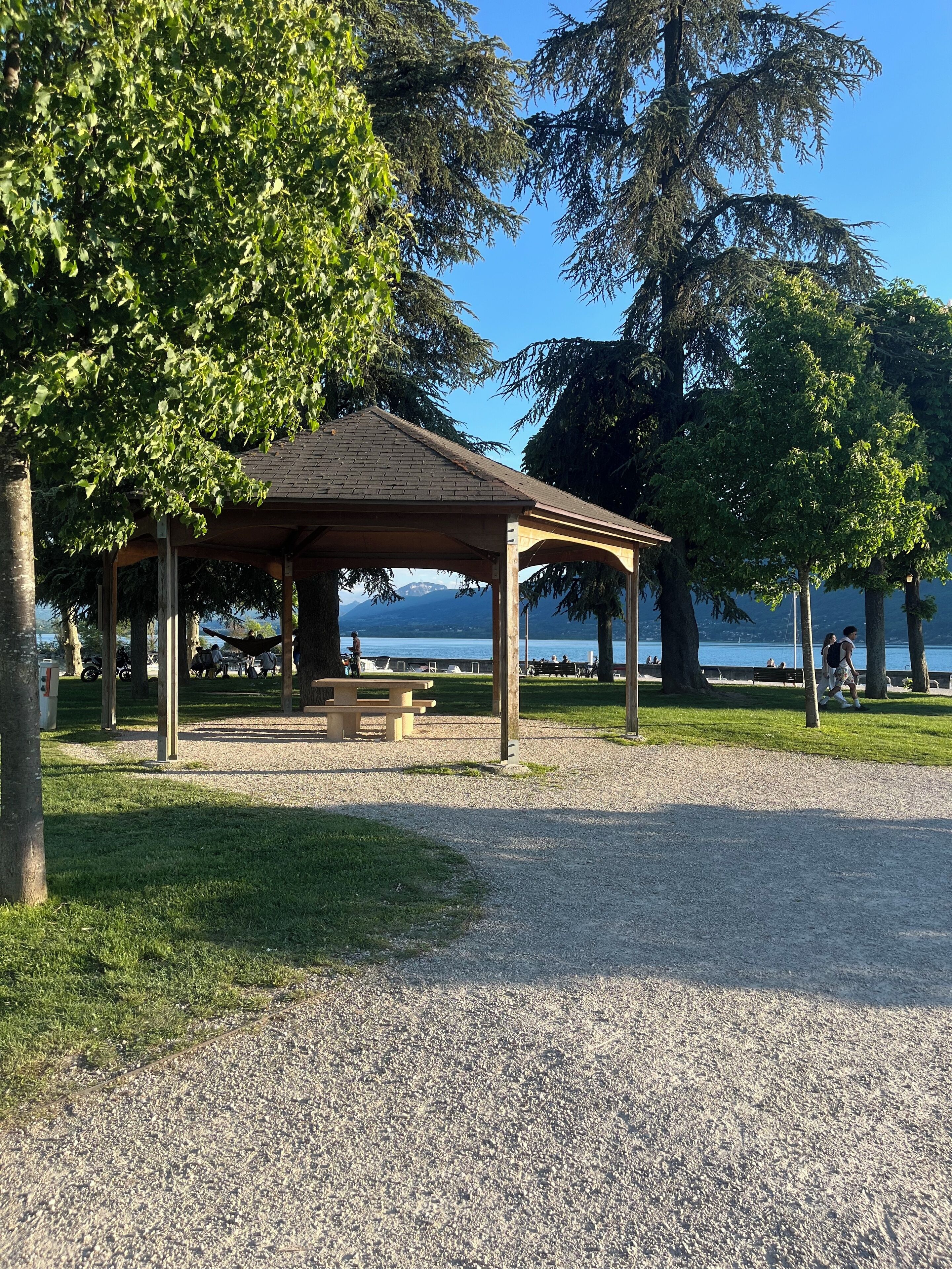 Ein Pavillon mit Kiesweg, umgeben von Bäumen und Blick auf einen See.