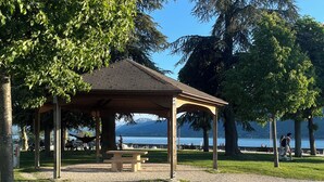 Un gazebo con un vialetto ghiaioso, circondato da alberi e vista su un lago.