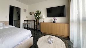 Habitación de hotel con cama, escritorio, televisor, un florero con flores y una mesa redonda.