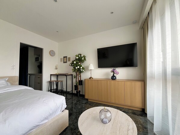 A hotel room with a bed, a desk, a TV, a vase with flowers, and a round table.