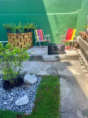 Un espace patio agrémenté de deux chaises colorées, d’un petit arbre et d’un mur en pierre.