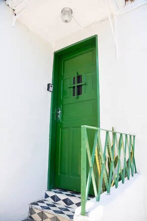 Une porte verte avec un portail en métal devant, le tout adossé à un mur blanc.