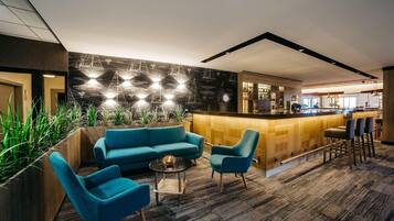 Un'area bar moderna con un bancone in legno, sgabelli da bar e una zona salotto con divano e poltrone.
