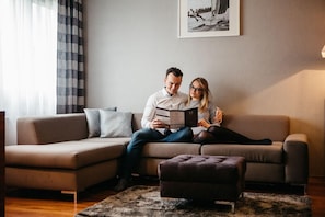 A couple sitting on a sofa with a framed picture on the wall, a small ottoman, and a patterned rug.