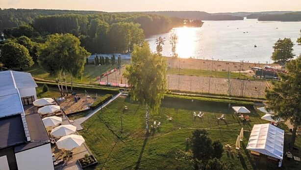 A riverside view with a grassy area, trees, and a building with outdoor seating. - Novotel Olsztyn (Olsztyn)