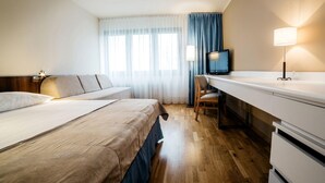 A hotel room with two beds, a desk with a TV, a lamp, and a window with curtains. - Novotel Olsztyn (Olsztyn)