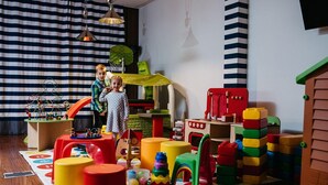 A playroom with various toys, a playhouse, and a striped curtain. - Novotel Olsztyn (Olsztyn)