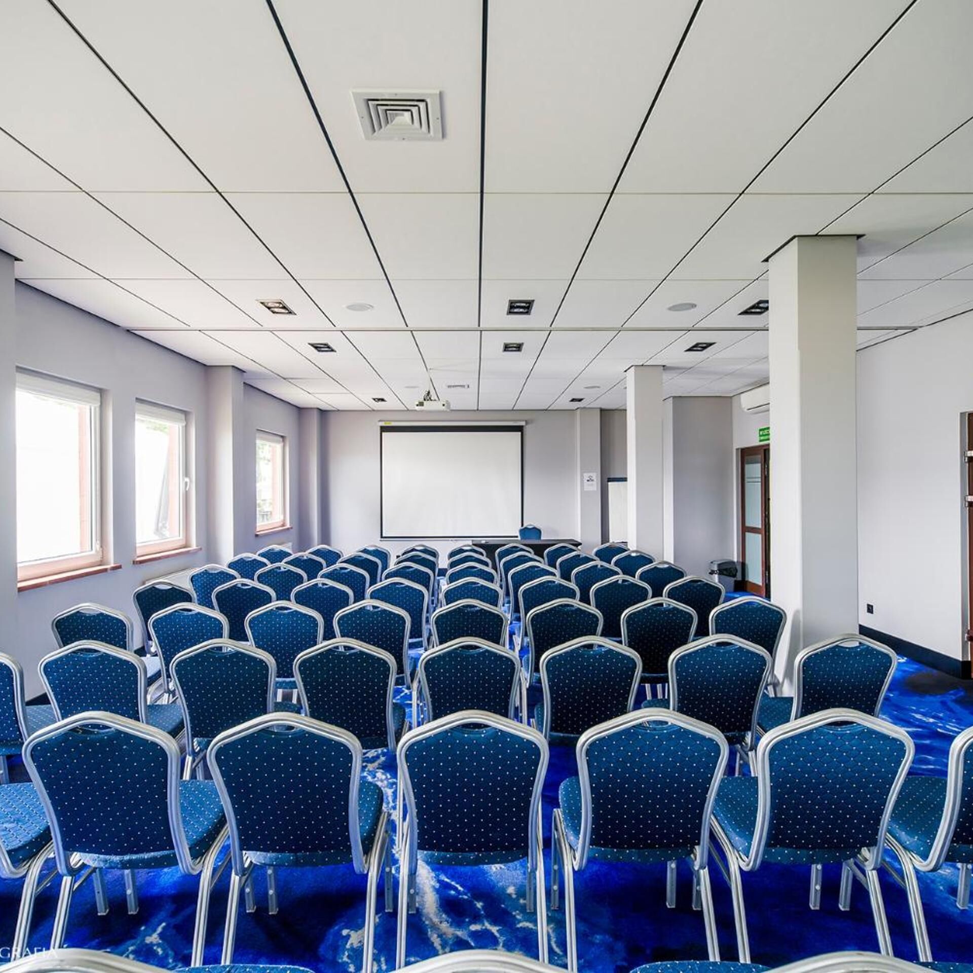 A conference room with rows of chairs, a projector screen, and windows.