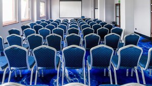 Une salle de conférence avec des rangées de chaises, un écran de projection et des fenêtres.
