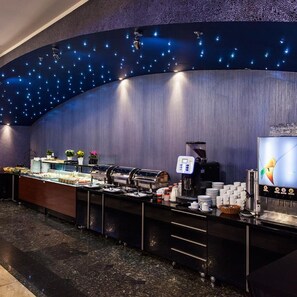 Een buffetgedeelte met een gebogen muur, plafondlampen en een koffieapparaat.