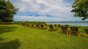 Une rangée de chaises longues en bois sur une pelouse verdoyante, avec un lac et des arbres en arrière-plan.