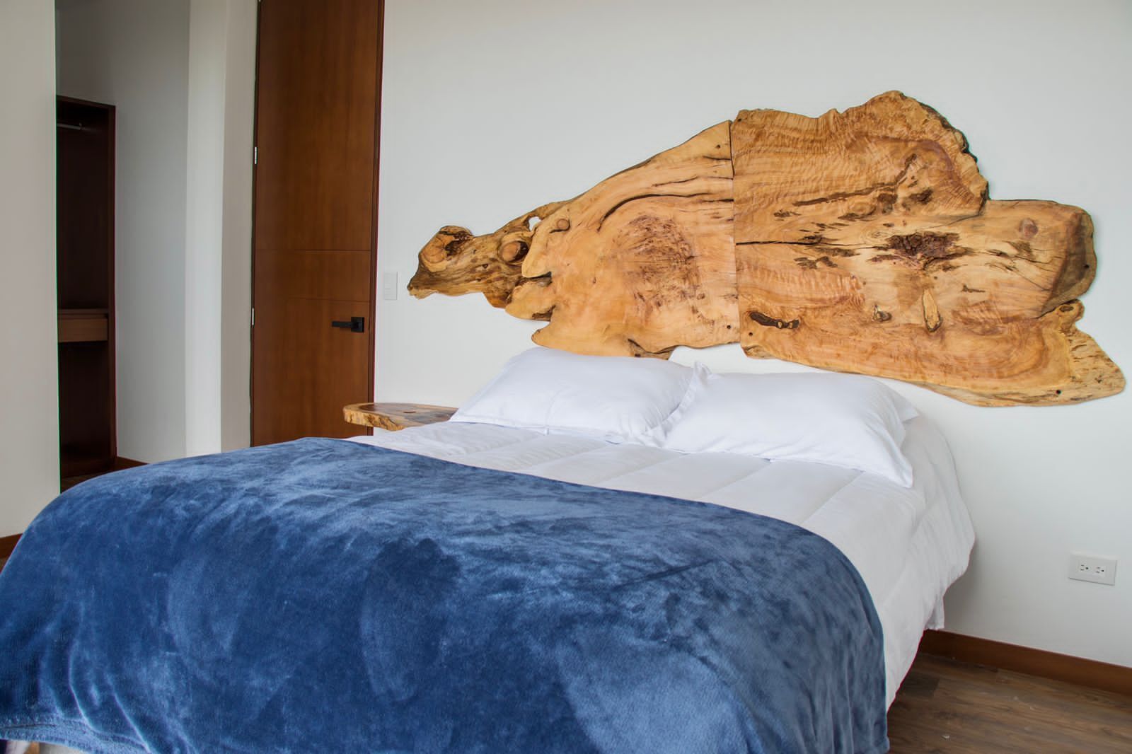 Une chambre à coucher avec une grande tête de lit en bois, un lit recouvert de draps blancs et une couverture bleue.