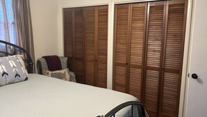 Ein Schlafzimmer mit einem Bett, einem Sessel und einer Holztür, die sich seitlich öffnen lässt.