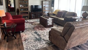 Ein Wohnzimmer mit einem roten Sofa, einem braunen Sofa, einem Fernseher und einem Bücherregal.